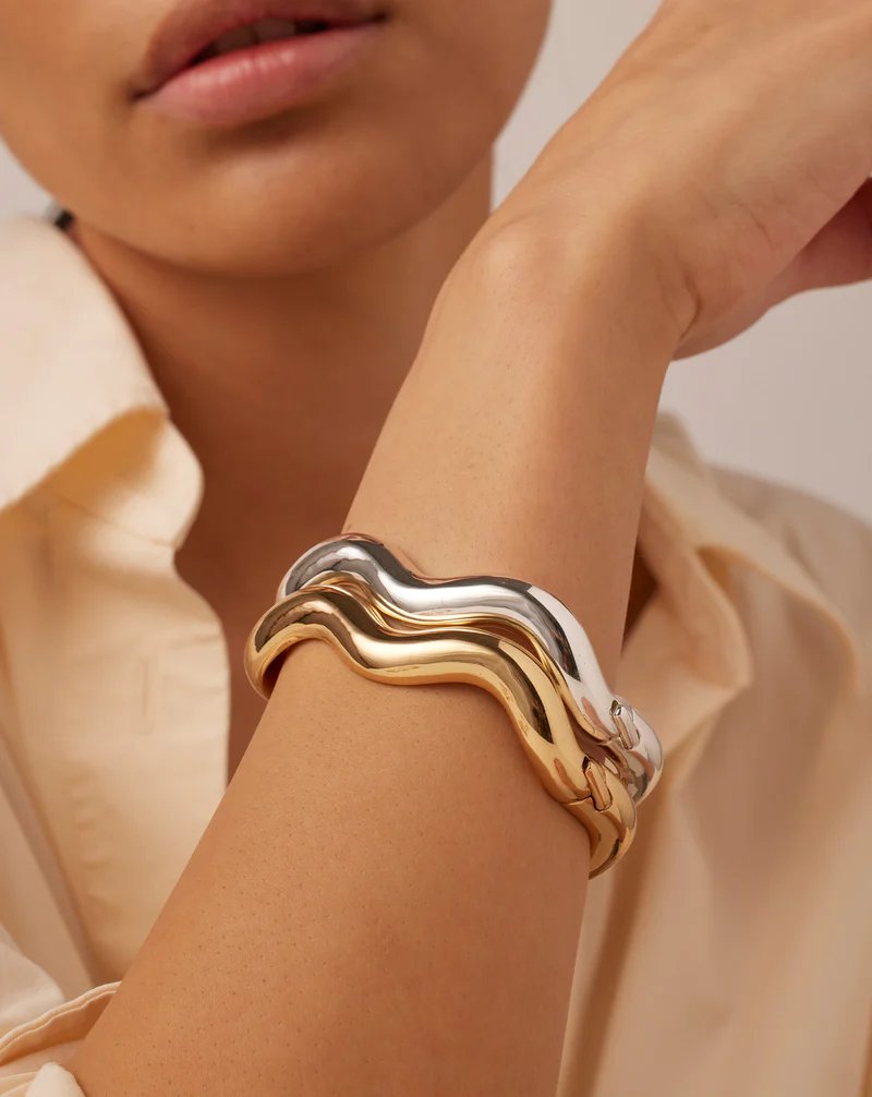 Jenny Bird Ola bangle in high polish gold. Curved gold bangle with a hinge and tab lock closure, styled as a stack of two on model's arm.