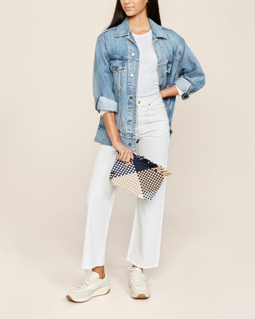 Model wearing the Naghedi havana clutch in graphic geo somerset, denim jacket, and white jeans and top.