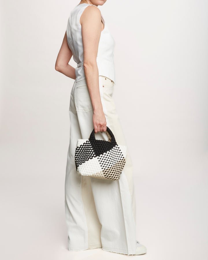 Model holding the Naghedi St. Barths small tote graphic geo in palermo print. Black, white and tan woven print bag with black strap.