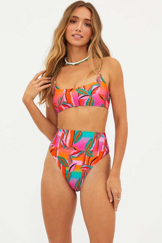 Model wearing Beach riot highway bottom in palm beach. High waisted bikini bottoms in multicolored print including pink, blue, green, red, purple and orange.