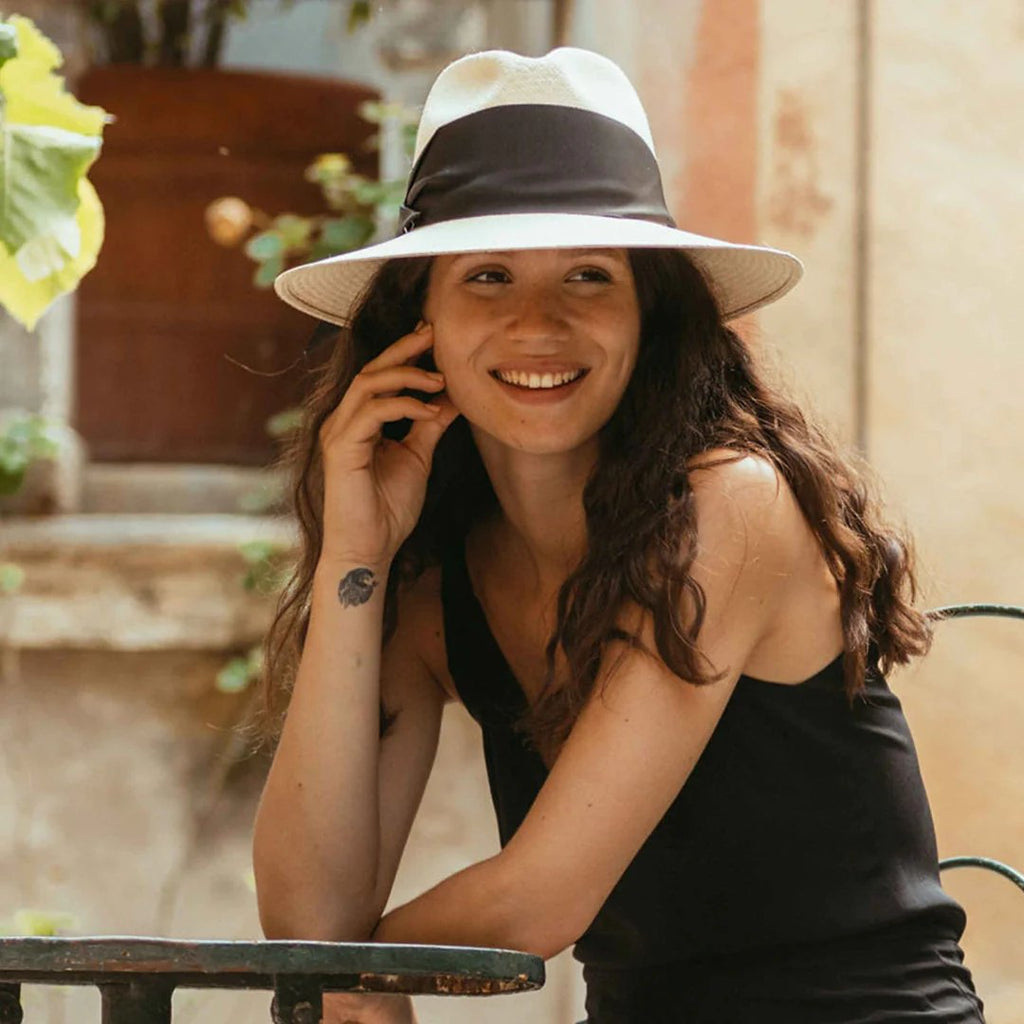 Women's Freya natural straw fedora with broad brim and oversized black grosgrain band, wrapped asymmetrically around the hat and finished with a modern angular fold.