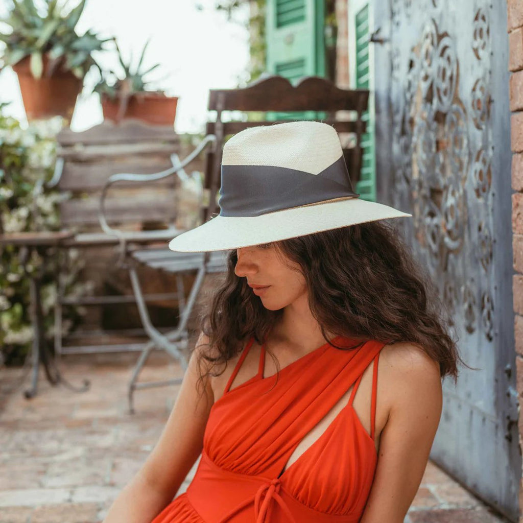 Women's Freya natural straw fedora with broad brim and oversized black grosgrain band, wrapped asymmetrically around the hat and finished with a modern angular fold. Side view while styled on model.